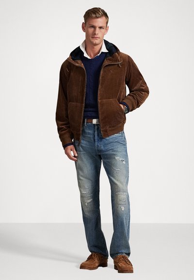 Brun kordfløjljakke med hætte; marineblå kabelstrikket sweater underneath; slidte blå jeans; brune sko. Har foran lommer og en lynlås.