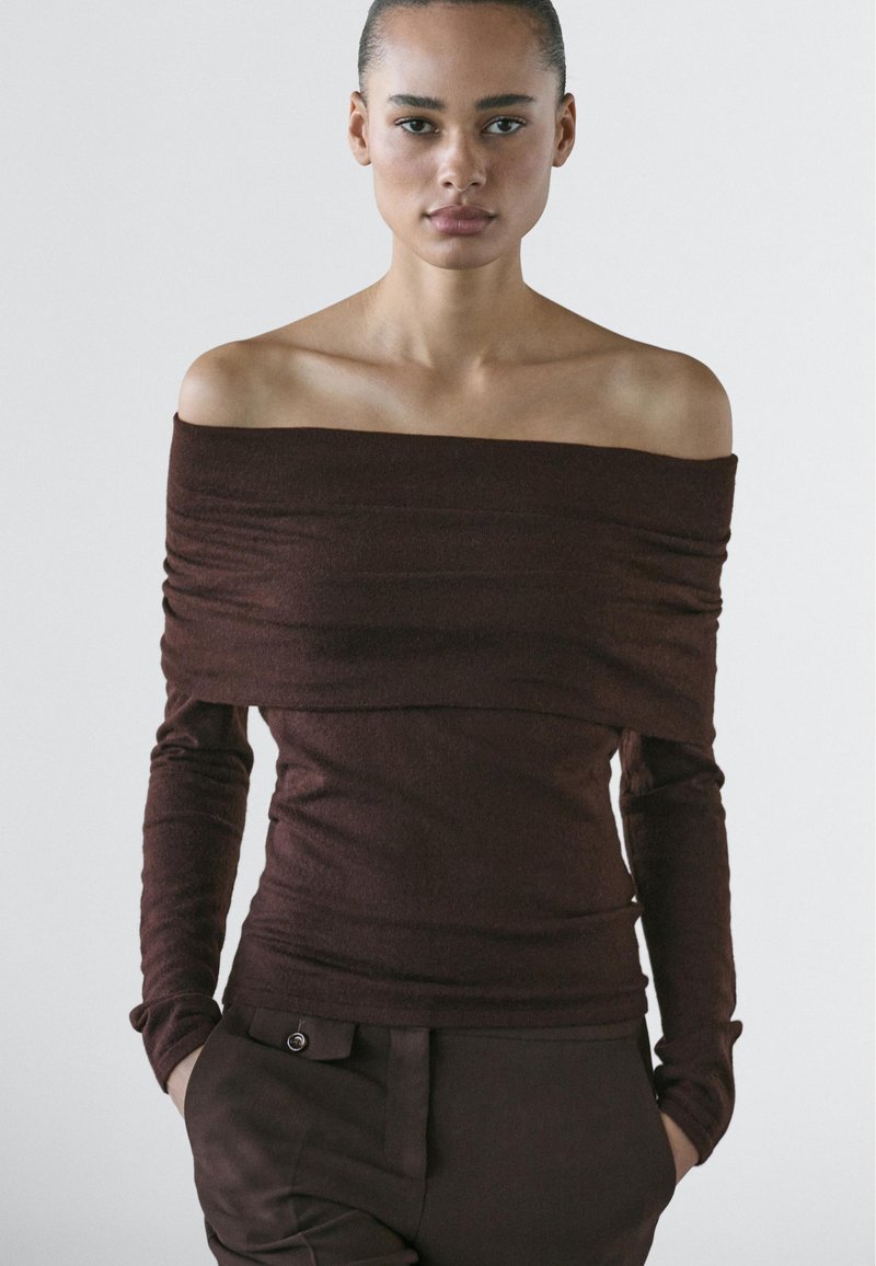 Brown off-shoulder top made of soft fabric with long sleeves, featuring a fitted design and subtle texture. Paired with matching pants.