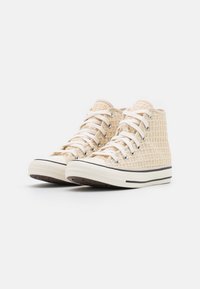Wysokie trampki z jasnobeżowej, tkaninowej tkaniny z białymi sznurowadłami, gumowymi podeszwami i czarnymi akcentami na śródpodeszwie. Uwaga: teksturowana powierzchnia.