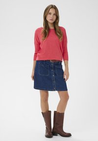 Pull-over corail, jupe trapèze en denim avec fermeture à boutons et poches, bottes marron montantes jusqu'aux genoux. Design simple avec texture lisse.