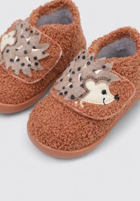 Zapatillas de casa marrones y esponjosas con diseño de erizo, que cuentan con un tejido texturizado, cierre de banda elástica y un suave forro interior en contraste.