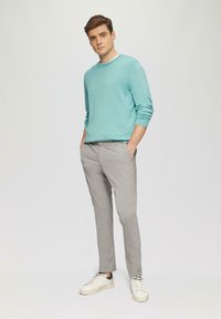 Jasnoniebieski sweter z okrągłym dekoltem, zestawiony z jasnoszarymi spodniami i białymi sneakersami. Prosty design, gładka tkanina i dopasowany krój.