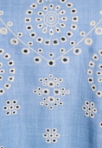 Tessuto azzurro chiaro con ricami bianchi, caratterizzato da motivi circolari e floreali, e cuciture di accentazione nera in tutto il design.