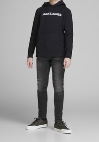 Sudadera marinera con el logo blanco de "JACK & JONES", bolsillo frontal, combinada con jeans slim-fit de color gris oscuro y zapatillas verde oscuro con suelas blancas.