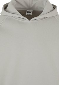Lys grå hettegenser laget av myk fabric, med snorhette, rund hals og raglanermer med synlige sømdetaljer.