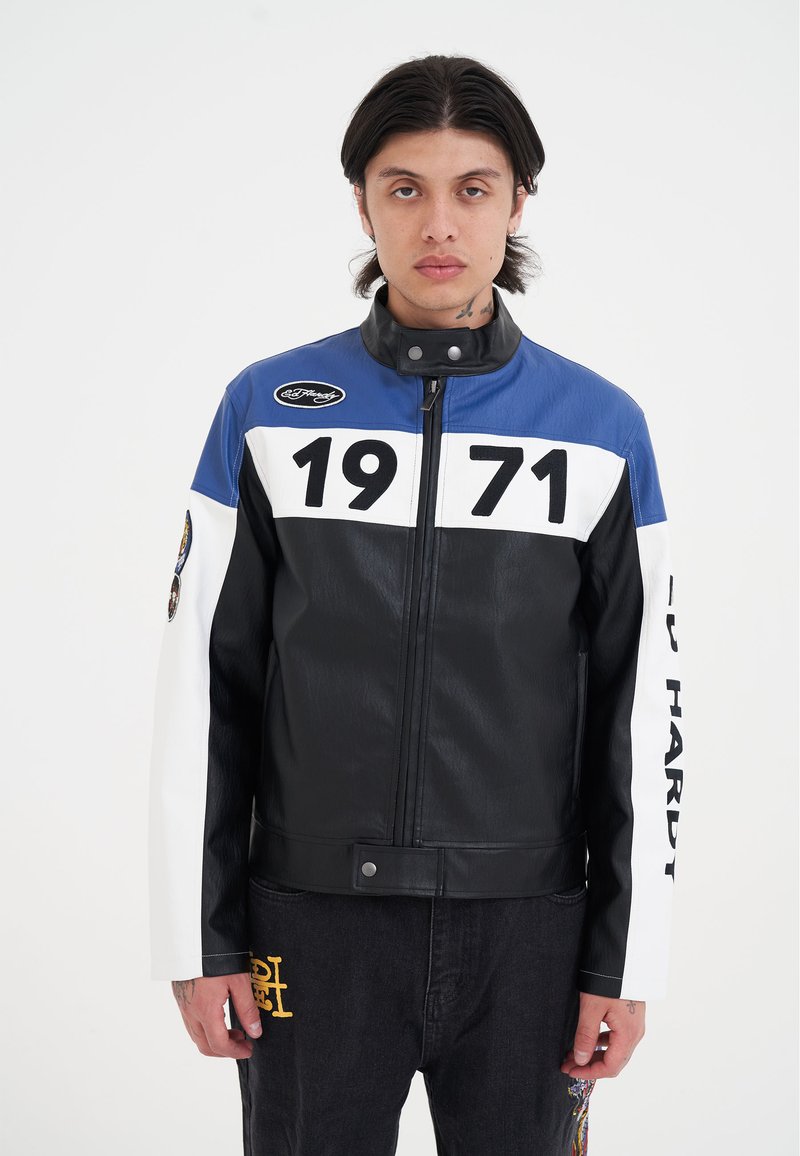 Svart och blå läderjacka med vita detaljer, med djärva siffror "1971" och varumärke på ärmarna. Texturerad yta, dragkedjestängning och tryckknapp.
