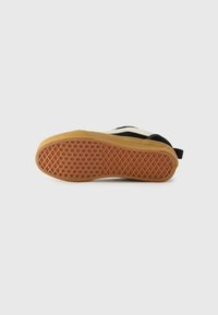 Sneaker nera e crema con suola in gomma testurizzata. Presenta un motivo a nido d'ape e un tassello sul retro per facilitare l'indossamento.