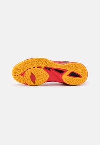 Sport shoe outsole featuring a black, red, and yellow rubber design with textured grip patterns and structural accents for traction.