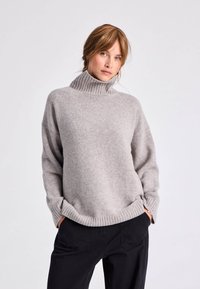 Šviesiai pilka turtlenecko megzta palaidinė su raukšlėmis apykaklėje ir priekyje. Pagaminta iš minkštos, tekstūruotos medžiagos; laisvas siluetas su nukirstomis pečių siūlėmis.