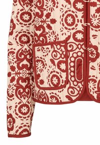 Manche et poche de veste matelassée avec des motifs floraux rouges et géométriques sur un fond crème, dotées de fermetures à boutons noués.