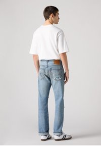 Lichtblauwe denim jeans met een rechte pijp, voorzien van een versleten ontwerp en een leren patch. Draag ze met een wit T-shirt en sneakers.