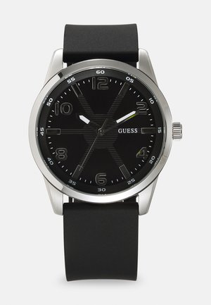 Montre en acier inoxydable argenté avec un bracelet en caoutchouc noir. Le cadran noir présente de grands chiffres, des aiguilles contrastantes et un motif texturé.