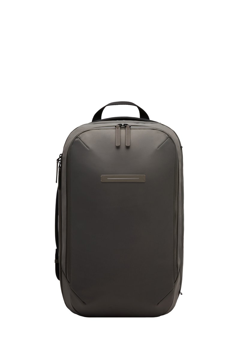 Sac à dos gris au design épuré, texture lisse, avec deux tirettes de fermeture éclair et un panneau avant minimaliste. Comprend une poignée supérieure et une poche latérale.