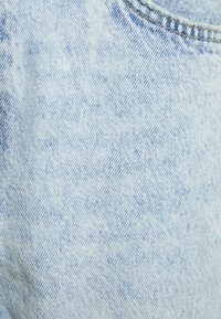 Hellblaue Jeansstoff mit einer leicht strukturierten Oberfläche, die ein dezentes Waschmuster und eine Standardnaht entlang der Kanten aufweist.