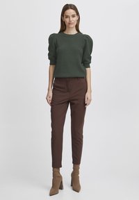Donkergroen sweater met textuurpatroon en pofmouwen, gecombineerd met bruine slim-fit broek en lichtbruine enkellaarsjes.