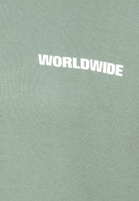 Mintgrünes Baumwoll-T-Shirt mit dem Wort "WORLDWIDE" in fetter weißer Schrift, die leicht gewölbt über den oberen Teil des T-Shirts verläuft.