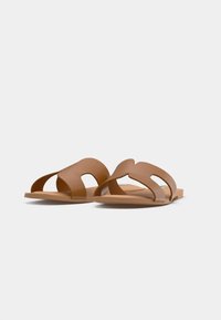 Sandales marron en matériau lisse, avec un design à bout ouvert comprenant des brides courbes et des sections découpées pour la circulation de l'air. Semelle plate.