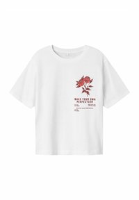 Balta īsām piedurknēm t-kreklā izgatavota no kokvilnas, ar sarkanu ziedu dizainu un tekstu "RADĪJIET SAVU PAŠU IDEĀLU" kopā ar papildu frāzēm.