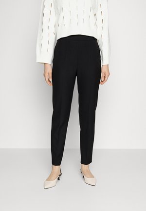Zwarte op maat gemaakte broek met een slim fit, met een gladde textuur. Draagt met een witte gebreide trui met uitsnijdingen en lichtbeige slingback schoenen.