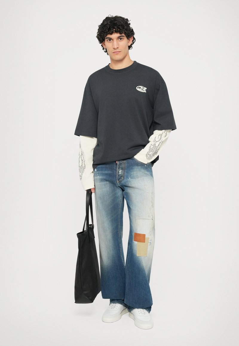 T-shirt nera in cotone con maniche corte e dettagli grafici. Jeans in denim blu chiaro con accenti in patchwork e orli sfrangiati. Borsa tote nera.