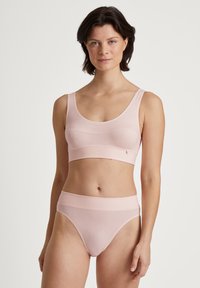 Brassière seamless rosa chiaro con spalline larghe e fascia di supporto, abbinata a slip a vita alta, che mostrano una texture morbida e liscia.