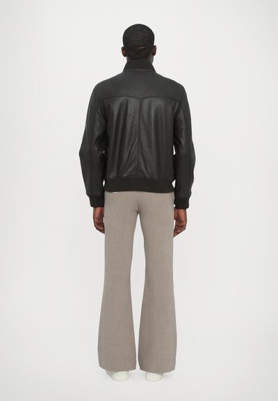 Chaqueta bomber negra de cuero con cuello y puños acanalados, combinada con pantalones de campana beige y zapatillas blancas. Textura suave con un diseño minimalista.