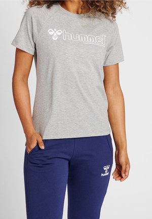 Personne portant un T-shirt gris à manches courtes et un pantalon bleu marine avec les logos de la marque Hummel visibles sur les deux.