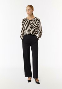 Schwarze hochtaillierte Hose kombiniert mit einer beigen und schwarzen gestreiften Bluse mit langen Ärmeln, die einen gerafften Ausschnitt und eine lockere Passform aufweist.
