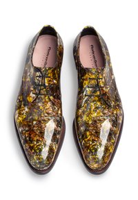 Chaussures habillées polies avec un motif marbré brillant marron et jaune, en cuir, à bout rond et avec des lacets noirs. Détail de la semelle extérieure marron.