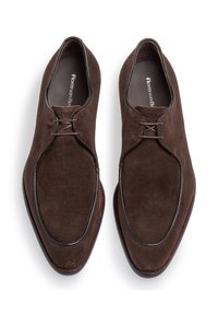 Scarpe da donna in suede marrone caratterizzate da una forma elegante con un profilo cucito e chiusura con lacci, poggiate su una suola con bordo rosso a contrasto.