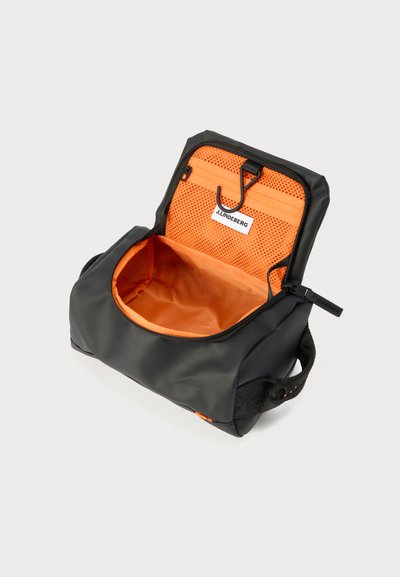 Μαύρη τσάντα ταξιδίου για είδη προσωπικής υγιεινής με έντονη πορτοκαλί εσωτερική επένδυση, τσέπη με φερμουάρ από δίχτυ και κόκκινο γάντζο στο ανοιχτό καπάκι.