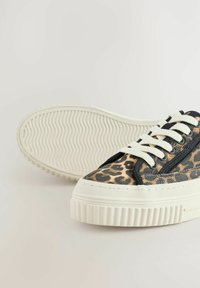 Tenisice sa printom leopard s teksturiranom platnenom gornjom stranom, kremastom gumenom potplatom i crnim vezicama, karakterizirajući ravni, širi oblik.