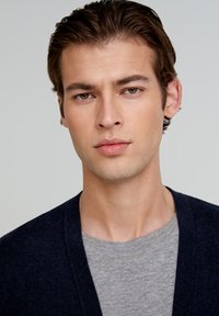 Marine cardigan over en grå crew-neck t-shirt. Modellen har kort, stylet hår og en neutral ansigtsudtryk. Glat hudstruktur.