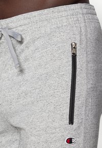 Grijze sweatpants van textiel, voorzien van een zwart ritszakje en een klein geborduurd logo op het onderbeen. Met een trekkoord in de taille.