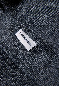 Dunkelgrauer Stoff mit strukturiertem Gewebe, das ein weißes Markenlabel mit der Aufschrift "LINDBERGH" enthält, das in den Stoff eingestickt ist.