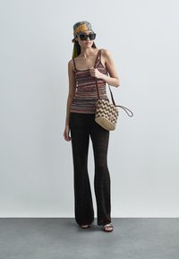 Czerwono-brązowy, bezrękawnik w paski, czarne rozszerzane spodnie z zygzakowatym wzorem, pleciona torba, okulary przeciwsłoneczne i kolorowa chusta na głowę.