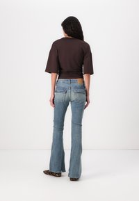 Brown cropped shirt with wide sleeves, paired with light blue flared jeans. Notable hardware includes two back pockets and a brown waistband label.
