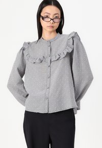 Grå randig blus med volangkrage, långa ärmar, knappstängning och små vita prickar; mjuk textur, avslappnad passform.