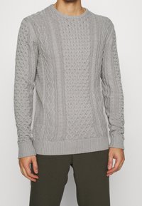 Jasnoszary sweter z dzianiny z wzorami w warkocze, z ribbanu w okrągłym dekolcie i mankietach oraz teksturowanym wzorem na całej powierzchni.