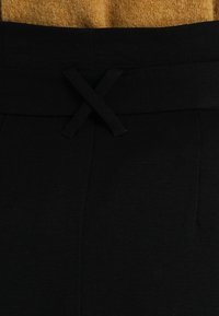 Pantalones negros con un acabado texturizado, que cuentan con un lazo en la cintura. El diseño incluye líneas limpias y un corte entallado.