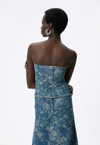 Denim bustier med blomstermønster; lyseblå farve; uden stropper design; sølv lynlås lukning bagpå; glat tekstur.