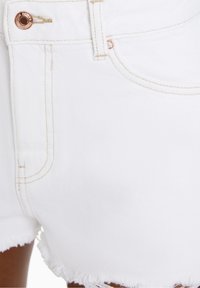 Weiße Denim-Shorts mit fransigem Saum, versehen mit beigen Nähten und einem kupferfarbenen Knopf. Nahaufnahme betont die Textur und die Details.