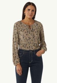 Lichtbruine blouse met patroon, een ronde halslijn, sleutelgatdetail en lange mouwen, gecombineerd met donkerdenim hoge taille jeans.