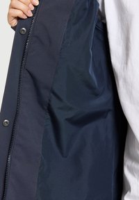 Veste bleu marine avec un intérieur lisse et texturé. Elle présente une fermeture éclair et des boutons-pression à l'avant, montrant une construction en couches.