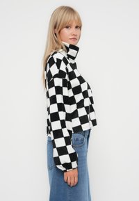Zwart-wit geblokte cropped fleece jas met hoge kraag en elastische manchetten, gedragen met blauwe denim jeans. Zacht en textuurmateriaal.