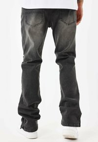 Zwarte spijkerbroek van denim met een vervaagde afwerking, rechte pijpen, twee achterzakken en lichte slijtage aan de zoom. Gecombineerd met witte sneakers.