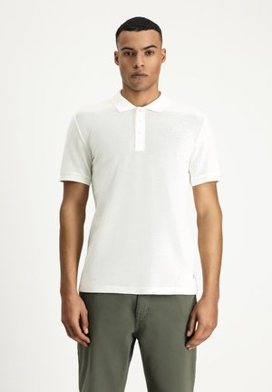 Weißes Poloshirt mit weicher Textur, kurzen Ärmeln, klassischem Kragen und Knopfverschluss, kombiniert mit grünen Hosen.