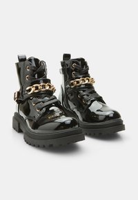 Botine din piele patent neagră, cu talpă groasă, având accente de lanțuri aurii și șireturi negre. Finish rezistent și texturat.