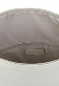 Interno di una borsa bianca con texture, dotato di fodera beige liscia, che presenta una tasca con zip e un'etichetta Gabor cucita all'interno.