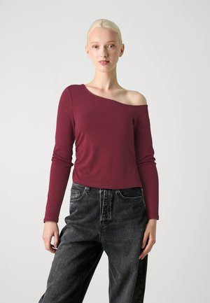 Bordeaux lange mouw top met een asymmetrische halslijn, gecombineerd met hoge taille zwarte jeans. Glad textuur, getailleerd silhouet.